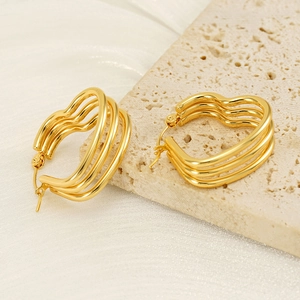 Three-layer wavy heart-shaped gold earrings on a textured stone platform