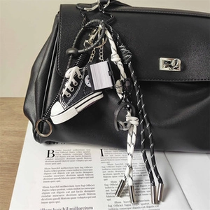 Dettaglio di mini sneaker in tela e ciondoli a libro su borsa in pelle nera
