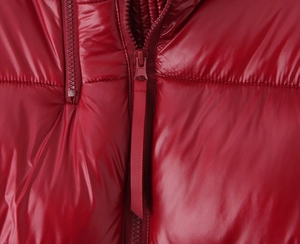 Detailed close-up of glossy red waterproof fabric and smooth zipper on puffer jacket