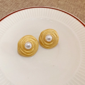 Détail de boucles d'oreilles vintage dorées en spirale avec perle blanche sur céramique