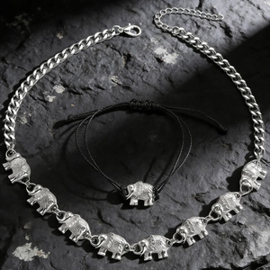 Detail of silver elephant charms on a cuban chain and woven bracelet over stone