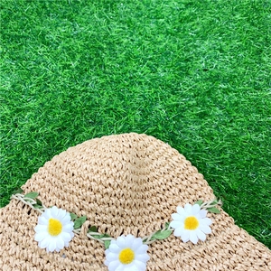 Detailed top view of handmade woven straw hat with daisy flower trim on green lawn