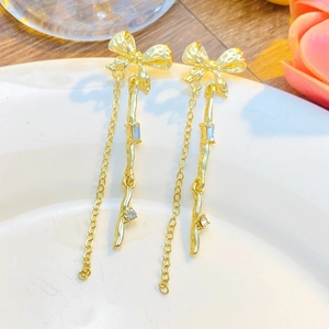 Macro detail of elegant golden bow tassel earrings with crystals on white ceramic