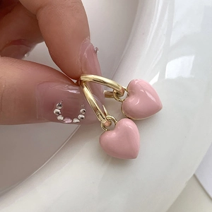 Détail de boucles d'oreilles dorées avec cœurs roses en émail portées à la main