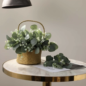 Artificial eucalyptus and white flower arrangement in a woven basket on marble table
