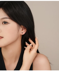 Close-up of small black flower stud earrings with five-petal design on a female ear