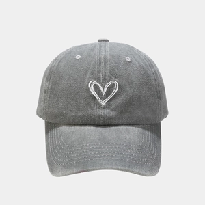 Close-up of white heart embroidery on a vintage washed grey cotton baseball cap