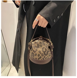 Detail of dark brown leather and leopard print jacquard barrel bag held by a model