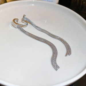 Detailed view of a silver tassel ear cuff with sleek metal chains in a white ceramic dish
