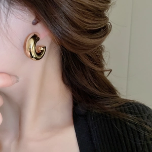 Close-up of minimalist chunky golden C-shaped hoop earring on model with metallic finish