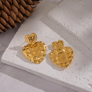 Detailed macro of golden hammered heart earrings on a natural white stone base