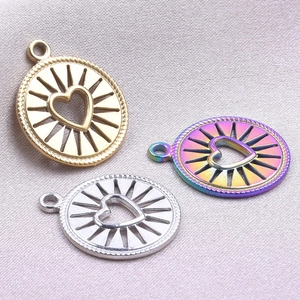 Three circular heart pendants in gold, silver and rainbow colors on beige fabric background