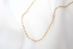 Vue macro d'un collier chaîne trombone doré sur un tissu texturé blanc élégant