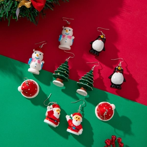 Flat lay of Christmas earring set with snowman, penguin, and tree on festive background