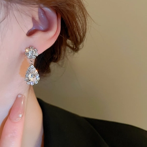 Close-up of a silver teardrop earring with crystals worn by a model in warm light