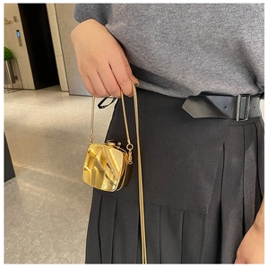 Close-up of a glossy gold mini lipstick bag with a sleek metal chain strap on model