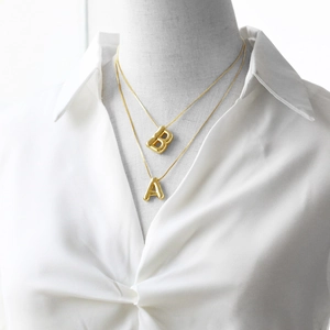 Detail of layered gold necklaces with 3D bubble letter pendants on a white shirt
