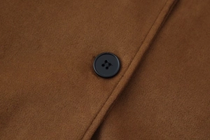 Macro detail of brown faux suede jacket featuring fine stitching and black button