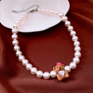 Detail view of pearl necklace with bear pendant on red silk background