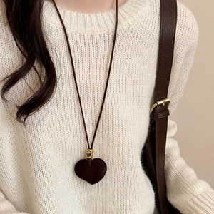 Detail of a brown flocked heart pendant necklace worn on a beige knit sweater