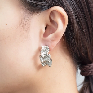 Gros plan sur boucle d'oreille froissée argentée avec texture métallique irrégulière
