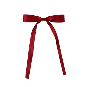 Close-up of a red satin ribbon bow hair clip with glossy finish and long streamers