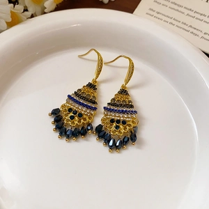 Detailed macro view of vintage gold tassel earrings with blue beads on white ceramic tray