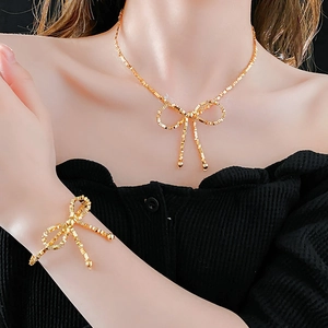 Close-up of a model wearing a gold bow necklace and bracelet set with black clothing