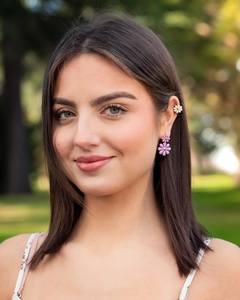 Detail of purple daisy earrings and white flower ear cuff worn on model in a park