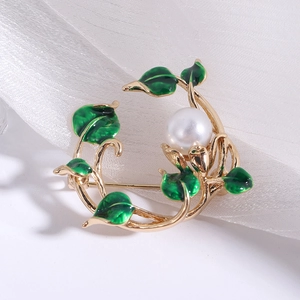 Close-up of a gold floral brooch with green enamel leaves and a large center pearl