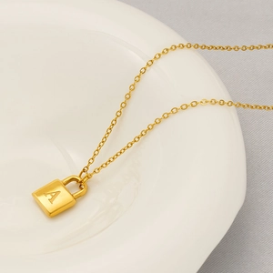 Minimalist gold necklace featuring a polished letter A padlock pendant on a ceramic dish