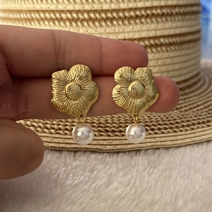 Detail of gold flower earrings with white pearl pendants held in hand for size
