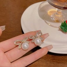 Dettaglio macro di orecchini a fiocco in argento con cristalli e perle bianche