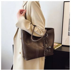 Detail of dark brown leather tote bag with white stitching and cute cat pendant