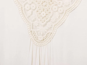 Macro view of delicate lace collar detail on white pleated cotton shirt for women