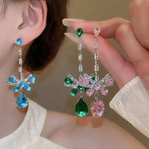 Detailed close-up of zircon bow and teardrop pendant earrings in blue, green and pink