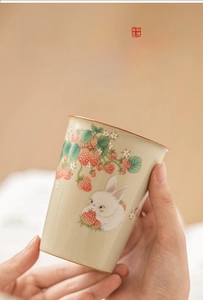 Close-up of celadon Ru kiln ceramic cup with hand-painted strawberry rabbit and gold rim