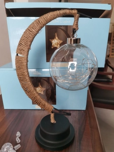 Detail of moon-shaped LED lamp with twine wrapping and glowing glass ball on wooden table
