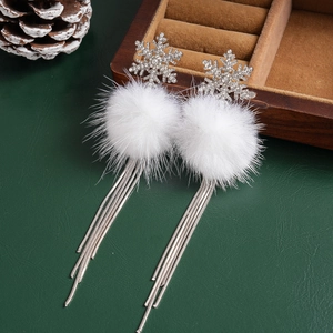 Silver snowflake earrings with white fur balls and rhinestone tassels on green background