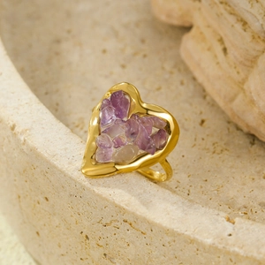 Detail of 18K gold-plated heart ring with purple natural stones on stone texture