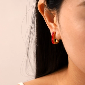 Detail of gold U-shaped hoop earrings with rectangular red gemstones on a model