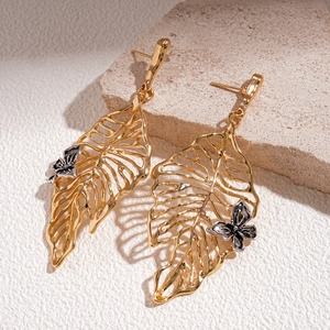 Detailed view of gold metal hollow leaf earrings with silver butterfly accents on stone