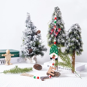 Close-up of wooden gnome ornaments with beads hanging on a snowy Christmas tree branch
