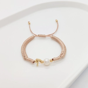 Detailed shot of braided bracelet with a white pearl and gold letter T pendant