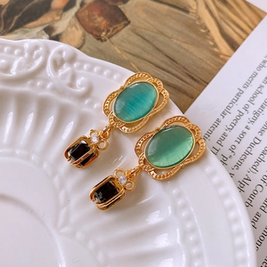 Close-up of vintage gold earrings with green cat-eye and black gems on a ceramic plate