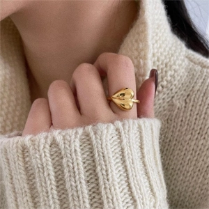 Close-up of a minimalist golden heart ring worn by a model in a cozy knit sweater