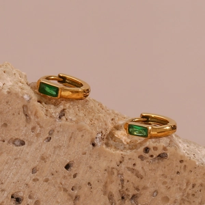 Gros plan de mini créoles dorées ornées de pierres rectangulaires vert émeraude