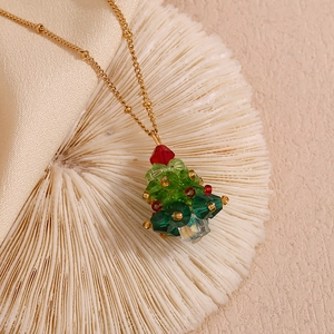 Detail view of a crystal Christmas tree pendant on a gold beaded necklace with 18K plating