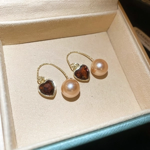 Détail de boucles d'oreilles dorées avec cœurs rouges et perles de champagne sur velours