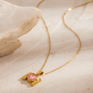 Close-up of vintage gold heart necklace with pink zircon on marble stone display